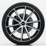 OEM car wheel next to aftermarket rim on white background